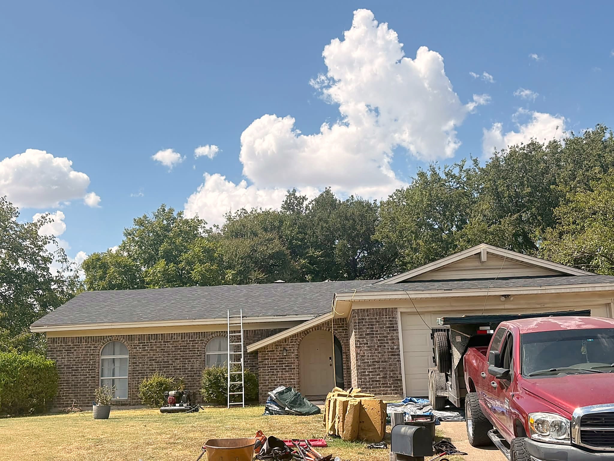 A single-story brick ranch in Benbrook with its new shingle roof finished and ladders still on the lawn