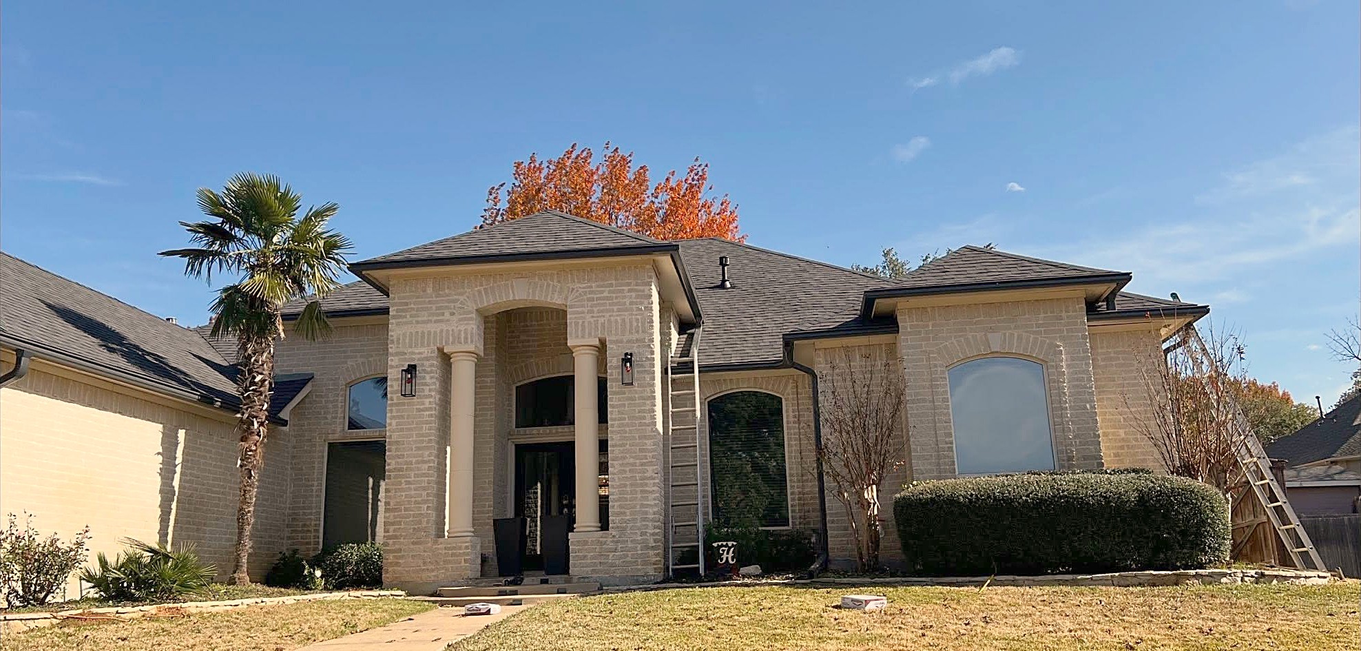 A cream brick home with a columned entry and a new charcoal shingle roof