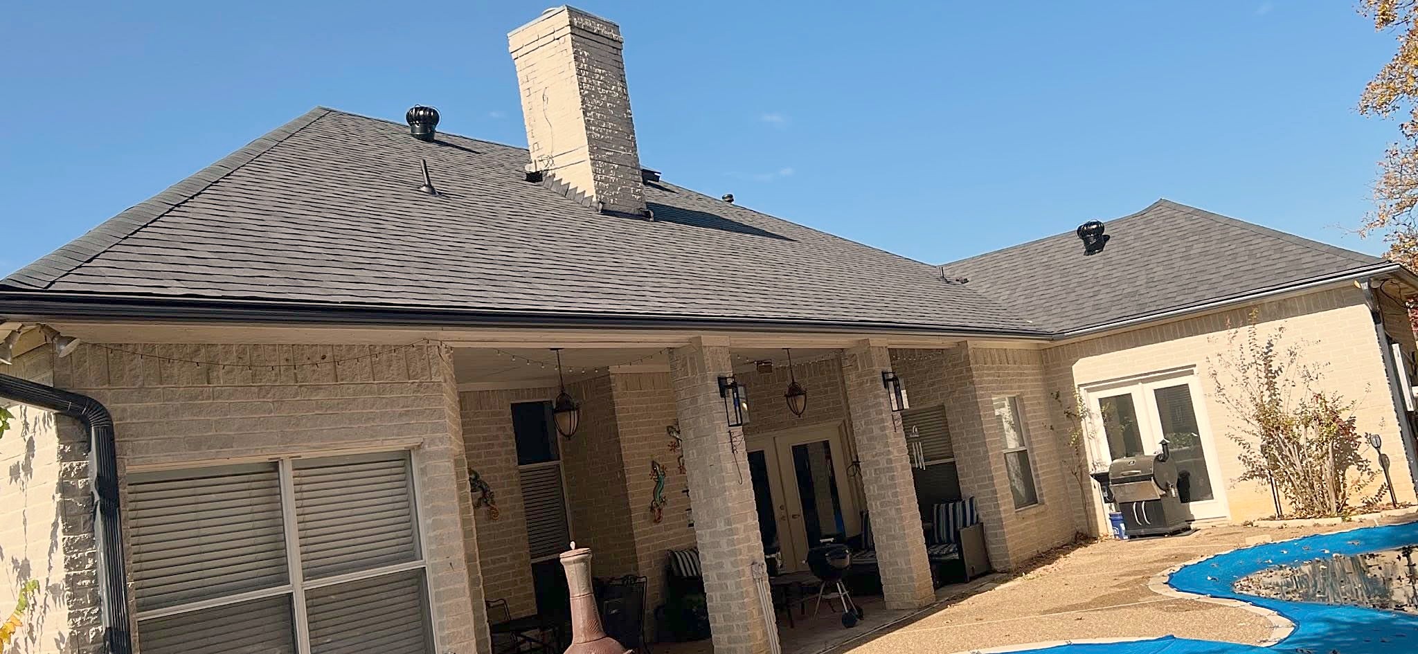 The rear of the cream brick home with its new charcoal roof over a covered patio and pool