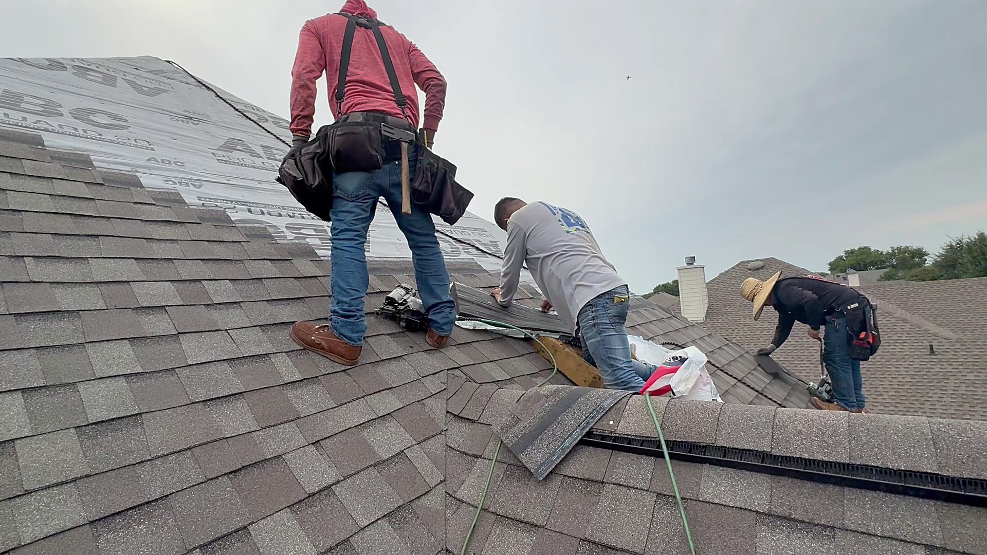 Three roofers laying a course of architectural shingles across a residential roof