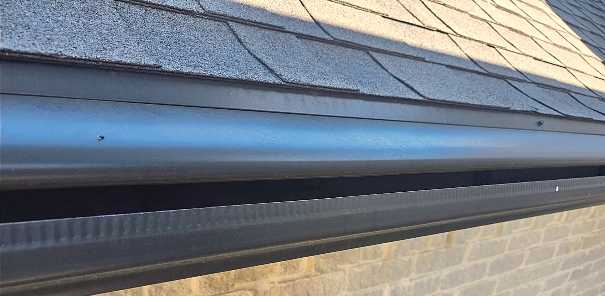 Close-up of a new black seamless gutter under the edge of new dark shingles