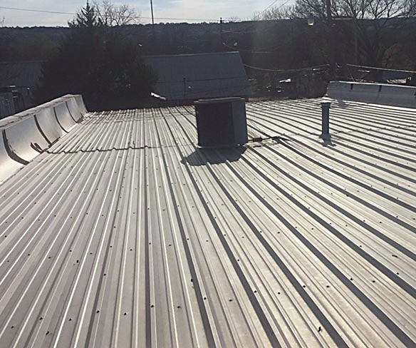 A standing seam metal roof on a low-slope section with a curb-mounted vent