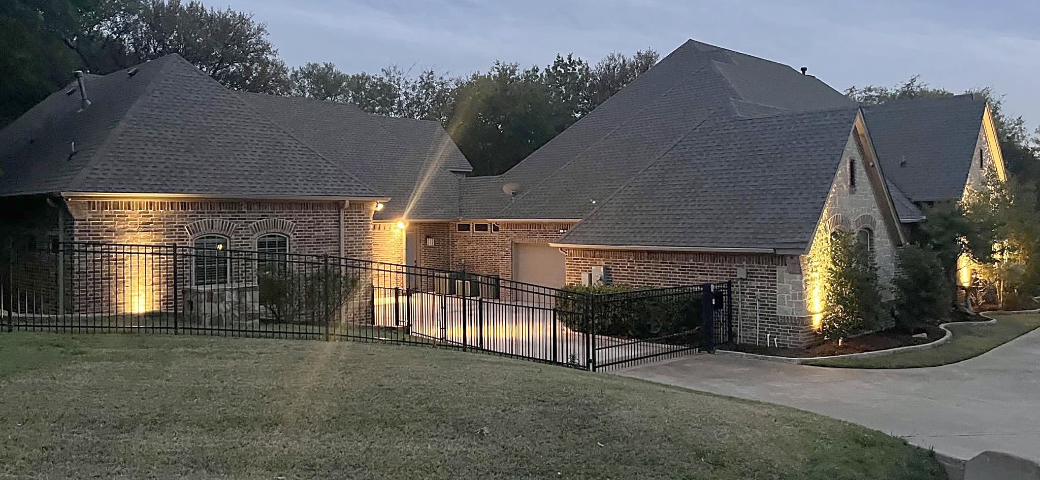A large brick home with a steep multi-gable dark shingle roof at dusk