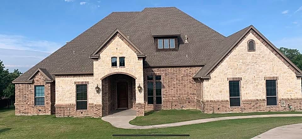 The same stone and brick home with its finished charcoal shingle roof