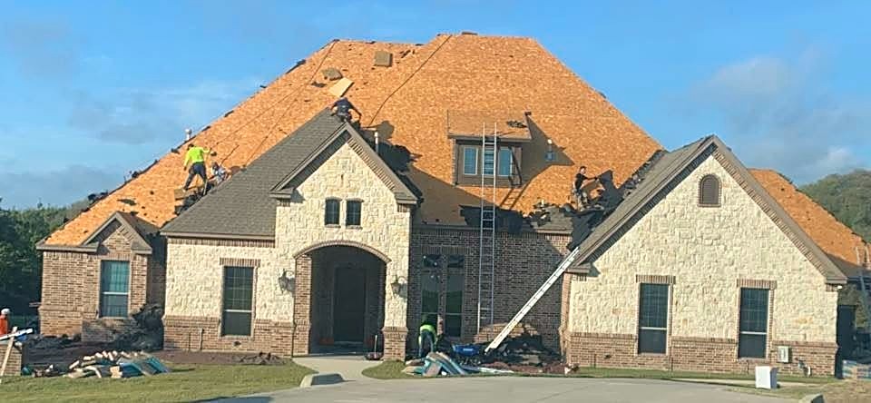 A large stone and brick home with new decking exposed and the crew on the roof