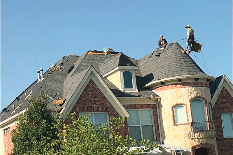 Two roofers tearing off an old green shingle roof on a steep stone turret
