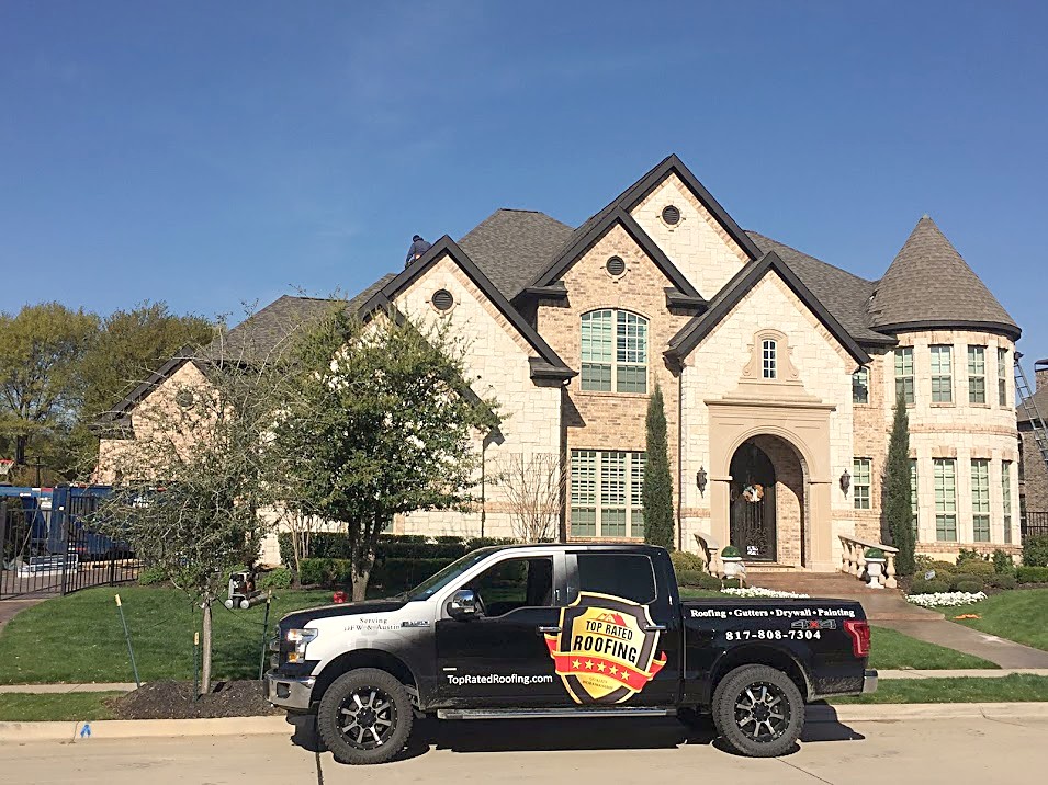 A branded Top Rated Roofing truck in the driveway of a large stone home after a reroof